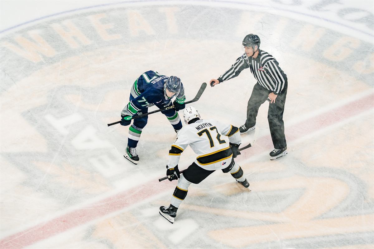 Two hockey players facing off at centre ice as the referee drops the puck